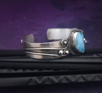 This unique piece features a breathtaking Larimar cabochon and two faceted Amethyst stones, adorned with intricate handcrafted waves. The gemstone is carefully set in a handcrafted sterling silver bezel, making it a true one-of-a-kind design. All Sterling Silver.