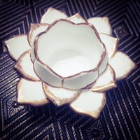 White ceramic flower-shaped object with gold trim on a dark patterned background
