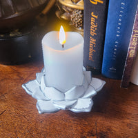 White candle in a lotus-shaped holder on a wooden surface with books in the background
