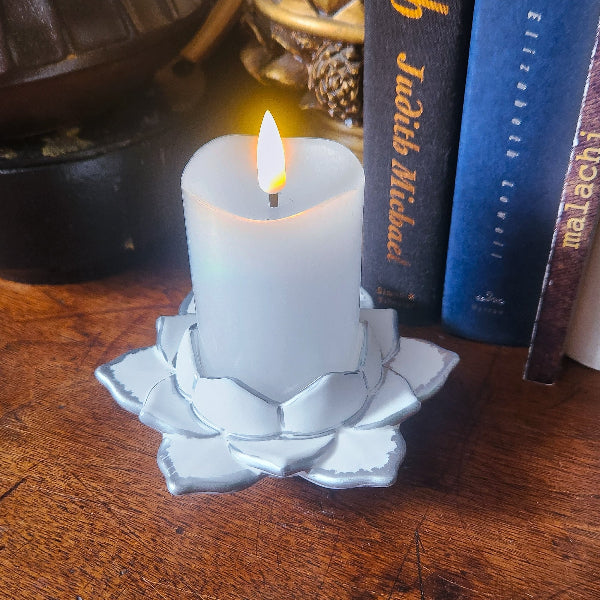 White candle in a lotus-shaped holder on a wooden surface with books in the background