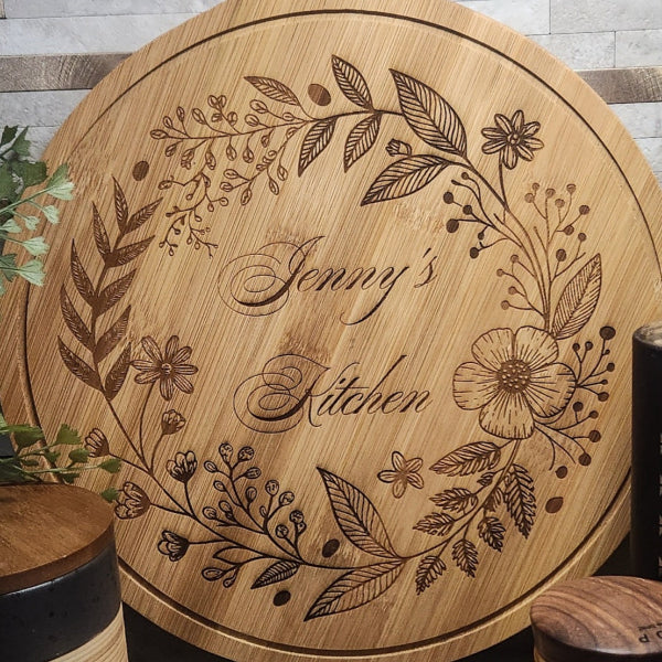 Wooden cutting board with engraved floral designs and 'Jenny's Kitchen' text.