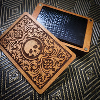 A wooden box with an ornate laser-engraved lid featuring a skull and floral scrollwork, shown next to an open lid revealing a black textured interior, set on a dark patterned surface.