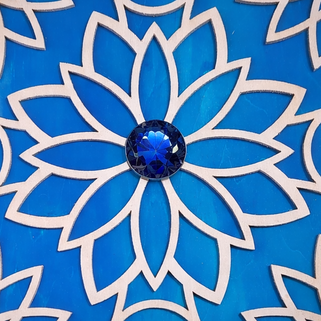 Decorative box with blue floral design and central gemstone on a textured surface