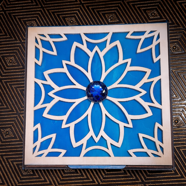 Decorative box with blue floral design and central gemstone on a textured surface