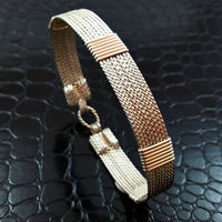 A twisted wire wrapped bracelet with a combination of silver and gold tones, displayed on a textured black background.