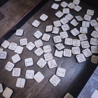 White wooden letter tiles scattered on a dark rustic wooden surface, with some tiles showing their engraved letter sides and others showing the blank back sides.