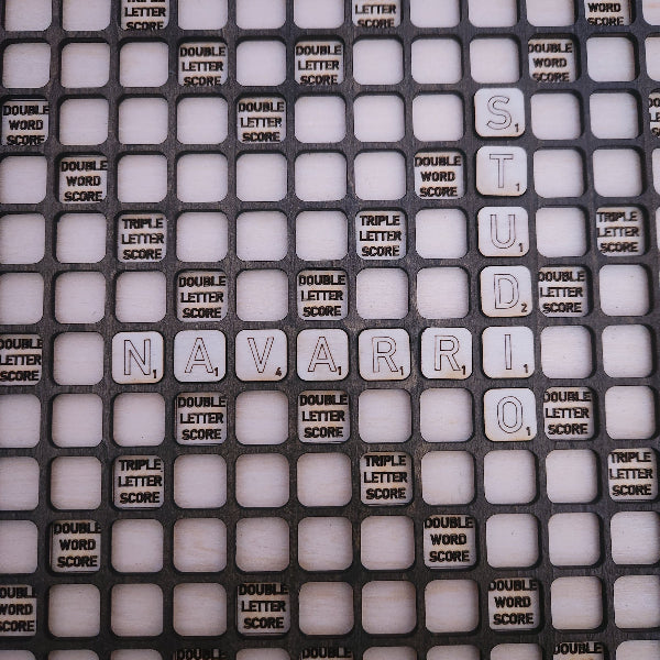 A close-up of a black Scrabble-style tile grid with white square tiles spelling out 'NAVARRIO' and many score tiles such as 'DOUBLE LETTER SCORE' and 'TRIPLE LETTER SCORE'.