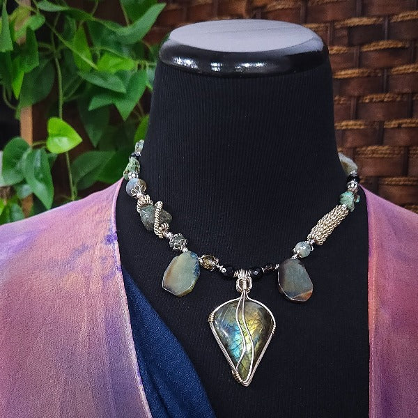 We all have a light within, an inner glow that others may see when they connect with our spirit. The shimmer and glow of this Labradorite Cabochon reminds me of this. This asymmetrical collar necklace is a testament to artisan craftsmanship and design. The Labradorite Cabochon is encased in a Wire Wrapped setting with a beautifully fluid look, and sterling silver coiled pieces add a unique look.