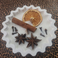 Candle in concrete bowl with Spices including a cinnamon stick, orange slice, cloves, and star anise