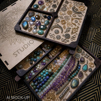 An open wooden jewelry and gemstone storage box filled with assorted jewelry-making supplies, including beads, stones, findings, and straws, arranged on a dark patterned fabric background.