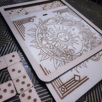 A wooden board game set featuring a decorative engraved board with a sun and moon design, shown with wooden dominoes on a patterned dark surface.