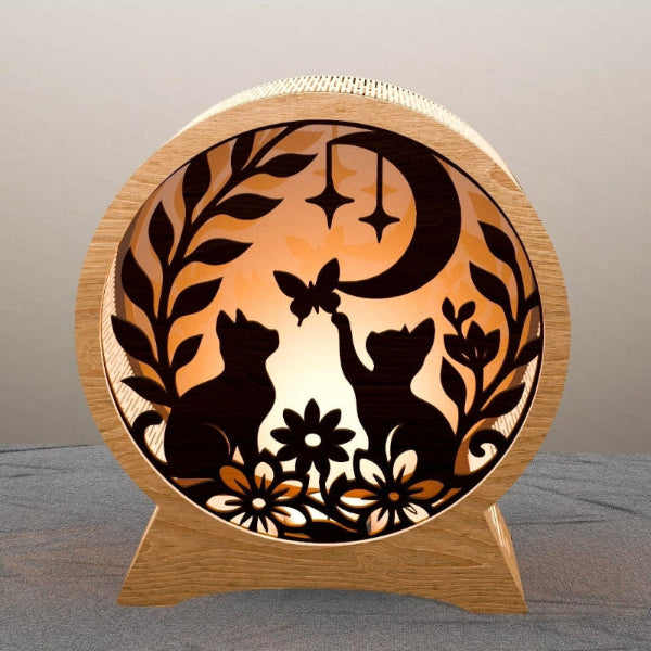 Wooden lamp with cut-out design of cats, flowers, and a moon on a gray surface.