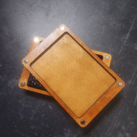 Two wooden rectangular trays or cards with rounded corners and metal rivets, stacked on a dark textured surface.
