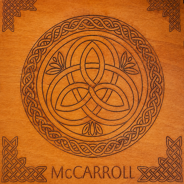 A square wooden plaque or box lid featuring a carved Celtic design, including a central triquetra knot inside a circular border, corner knot motifs, and the name 'McCARROLL' carved at the bottom.