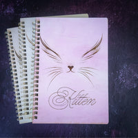 Notebook with cat design and 'Kitten' text on a dark textured surface