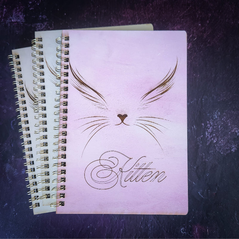 Notebook with cat design and 'Kitten' text on a dark textured surface