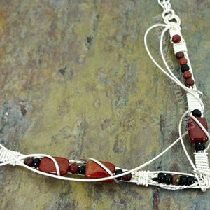 This collar is hand crafted and wrapped with strands of luscious sterling silver wire and embellished with Red Jasper and Black Onyx. Gemstones and accent beads are incorporated securely into the wire work. Flowing curves soften the hard lines of the metals and an asymmetrical flair makes this an unusual and dramatic addition to your private collection.