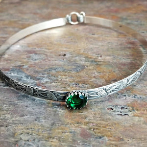This artisanal collar, boasting Soft and Sweet floral patterning, is crafted from sterling silver, and features a hand-set 12 x 10mm simulated emerald gemstone set into a sterling silver bezel.