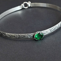 This artisanal collar, boasting Soft and Sweet floral patterning, is crafted from sterling silver, and features a hand-set 12 x 10mm simulated emerald gemstone set into a sterling silver bezel.