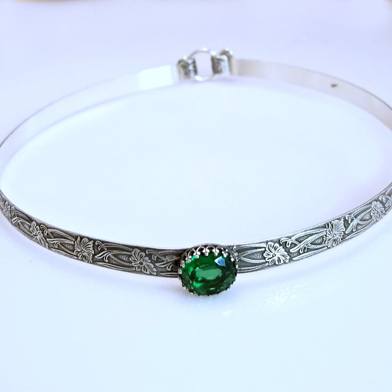 This artisanal collar, boasting Soft and Sweet floral patterning, is crafted from sterling silver, and features a hand-set 12 x 10mm simulated emerald gemstone set into a sterling silver bezel.