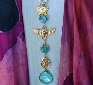 The scent of lavender and roses in the evening breeze. Golden sandals on the garden path. This garden themed necklace will glow with the reflection of the evening sun and garden torches. A chain of golden soft cornered squares and circles, a butterfly, a lunar moth and a sweet hummingbird medallion, all intermingle with faceted crystals in clear, pale blue, and aquamarine colors. Finished with a large, faceted blue crystal.